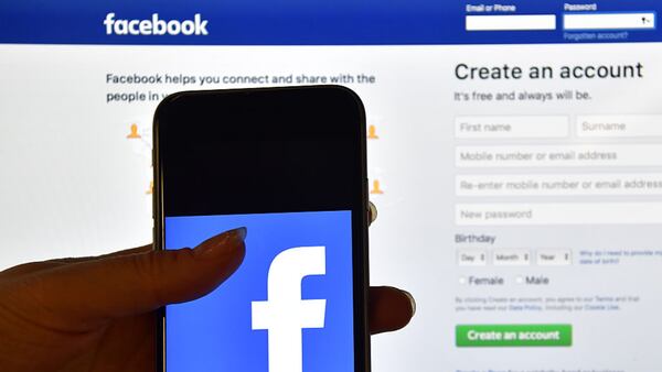 FILE PHOTO: A person holds an iPhone displaying the Facebook app logo in front of a computer screen showing the Facebook login page.  (Photo by Carl Court/Getty Images)