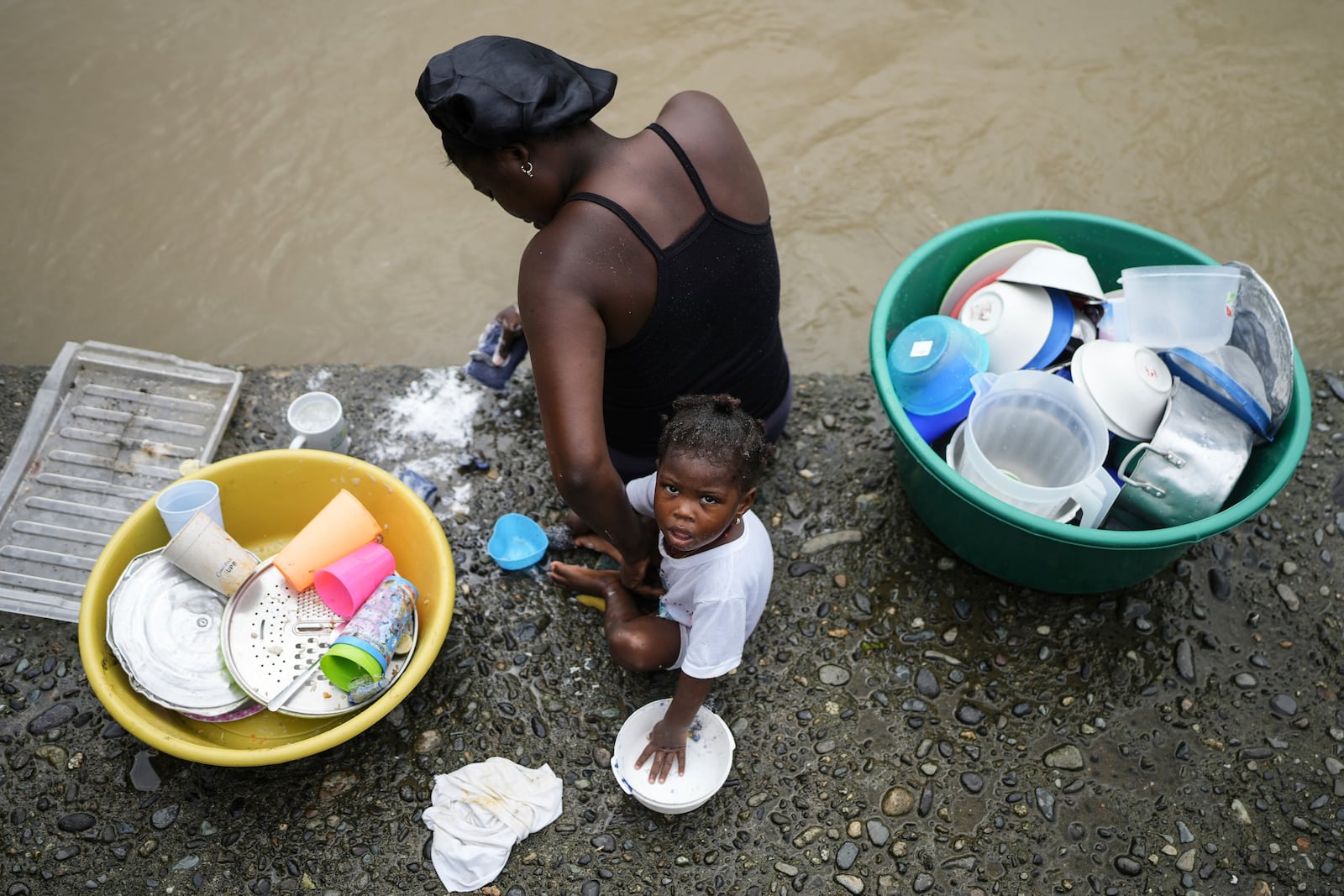 A mother and her baby wash dishes in the Atrato River, in El Arenal, Colombia, Thursday, Sept. 26, 2024. (AP Photo/Ivan Valencia)