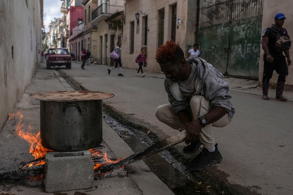 A man cooks soup over an open fire on a sidewalk, during a blackout in Havana, Cuba, Wednesday, Dec. 4, 2024. (AP Photo/Ramon Espinosa)