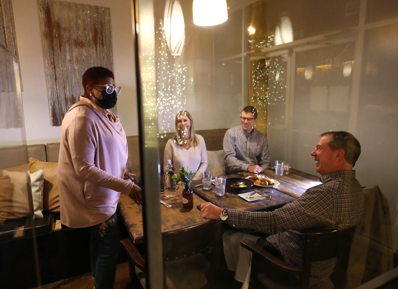 Deborah VanTrece, owner and chef of Twisted Soul Cookhouse, checks on diners Paul and Amanda Mayberry and their son Will during their evening meal inside a plexiglass cubicle at the restaurant on Dec. 9, 2020, in Atlanta.  (Curtis Compton / Curtis.Compton@ajc.com)