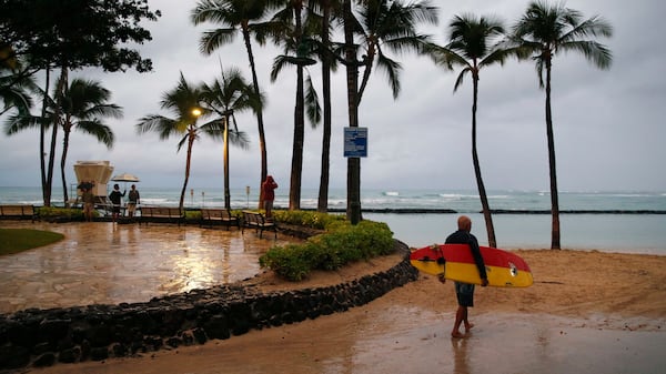 A surfer walks along Waikiki Beach in a light rain from Tropical Storm Lane, Saturday, Aug. 25, 2018, in Honolulu.