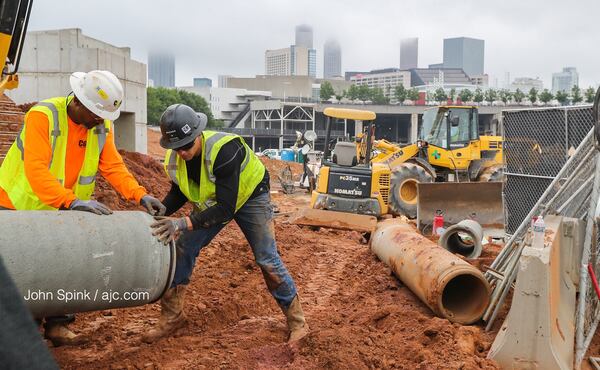 Fog covers downtown Atlanta as Reeves and Young Construction workers Joseph Jackson (left) and Tom Palmer put piping into place at the Home Depot Backyard next to Mercedes-Benz Stadium. JOHN SPINK / JSPINK@AJC.COM