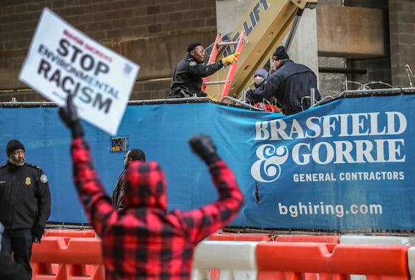 Two people locked themselves to construction equipment in Midtown to protest Atlanta’s planned public safety training center, causing a street to close amid the Monday morning commute, Jan. 29, 2024. The activists used reinforced bindings to lock their arms around the equipment at a Brasfield & Gorrie work site at 12th and Juniper streets. . (John Spink / John.Spink@ajc.com)

