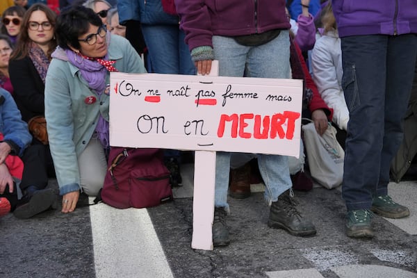 A woman sits by a placard reading " We are not born a woman but we die of it" during a women's rights demonstration, Saturday, Dec. 14, 2024 in Avignon, southern France, where the trial of dozens of men accused of raping Gisèle Pelicot while she was drugged and rendered unconscious by her husband is taking place. (AP Photo/Aurelien Morissard)