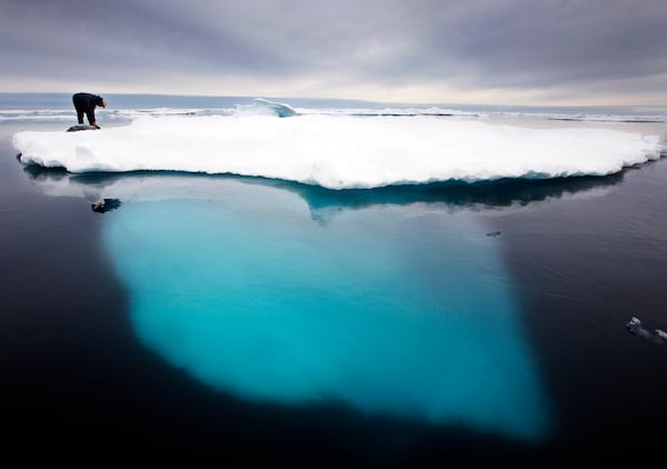 FILE - In this file photo dated July 2007, an Inuit seal hunter touches a dead seal atop a melting iceberg near Ammassalik Island, Greenland. (AP Photo/John McConnico, file)