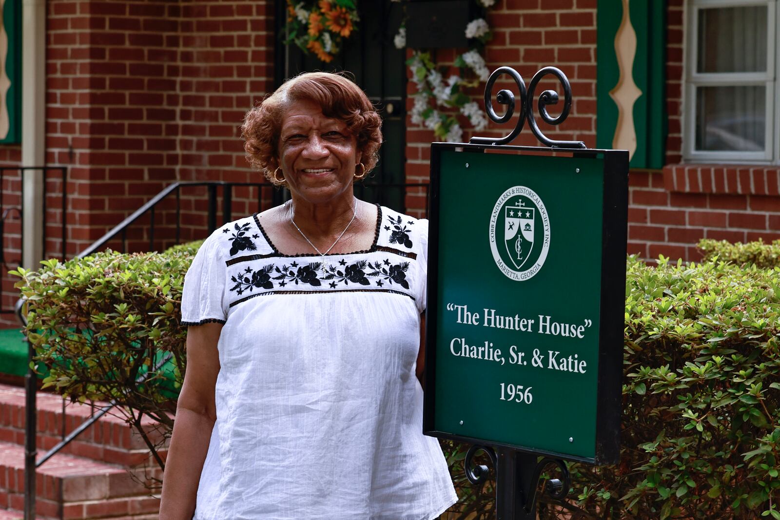 Mary Hunter Mullins, daughter of Charlie Hunter Sr. stands next to the marker placed in front of his home. The house is the first in a historic Black neighborhood to receive a home marker. (Natrice Miller/natrice.miller@ajc.com)