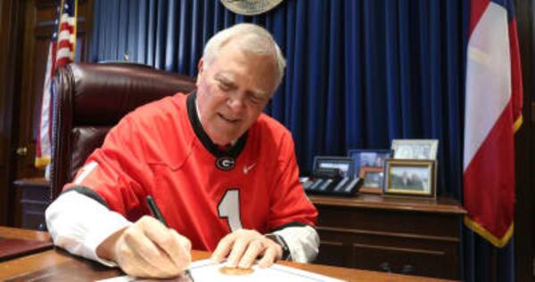 Gov. Nathan Deal, wearing a Georgia Bulldogs jersey, signs a proclamation supporting the football team before the 2018 national championship game. AJC FILE PHOTO