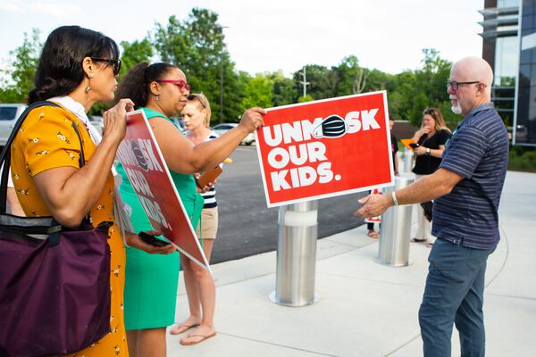 Billy Cahill (far right) hands a woman his "unmask our kids" sign to pose for a photo outside of the Cobb County School District office on  May 20, 2021, in Marietta, Georgia . Many community members waited in line to speak at the school board meeting to voice their support for unmasking.  CHRISTINA MATACOTTA FOR THE ATLANTA JOURNAL-CONSTITUTION