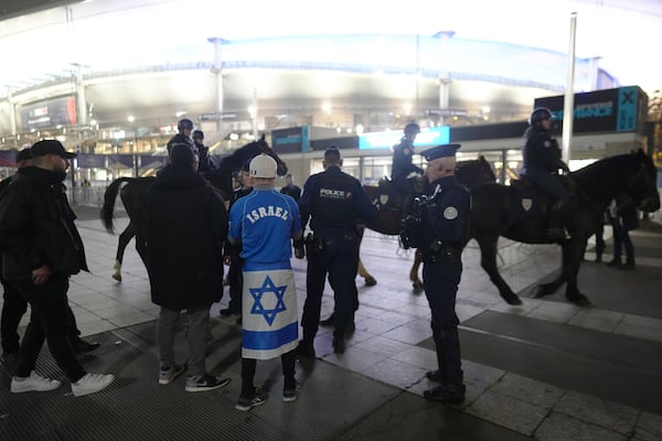 Police check a man covered with an Israeli flag next to the Stade de France before the UEFA Nations League soccer match between France and Israel, in Saint-Denis, outside Paris, Thursday, Nov. 14, 2024. (AP Photo/Thibault Camus)