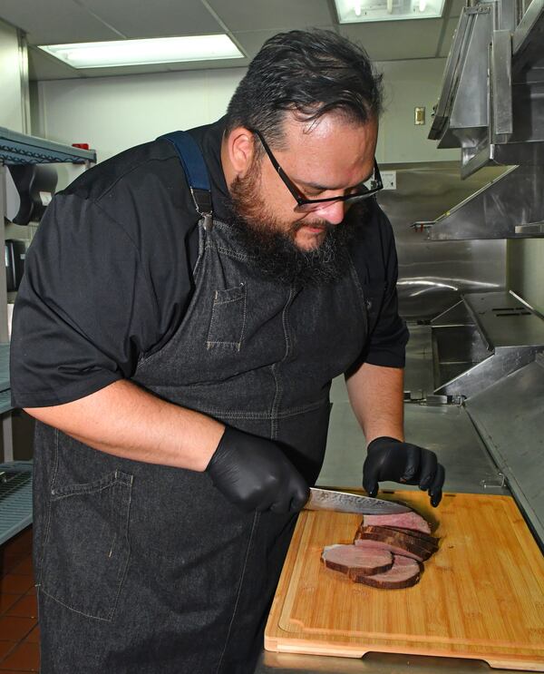 Chef Christian Lopez, whose family is from Colombia, slices eye of round steak for his Posta Negra Cartagenera (beef roast in the manner of the city of Cartagena). (Styling by Christian Lopez / Chris Hunt for the AJC)