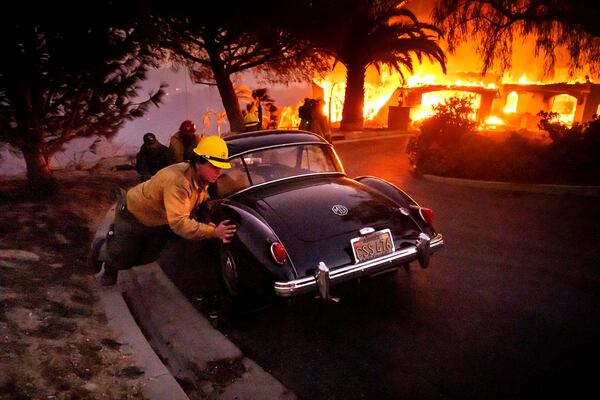 Firefighters and sheriff's deputies push a vintage car away from a burning home as the Mountain Fire burns in Camarillo, Calif., on Wednesday, Nov. 6, 2024. (AP Photo/Noah Berger)