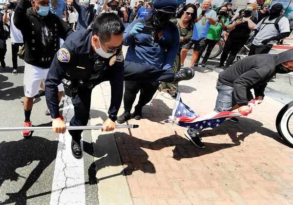 A young man steals an American flag from a White Lives Matter supporter as a Huntington Beach police officer tries to stop it during Black Lives Matter and White Lives Matter rallies in Huntington Beach.