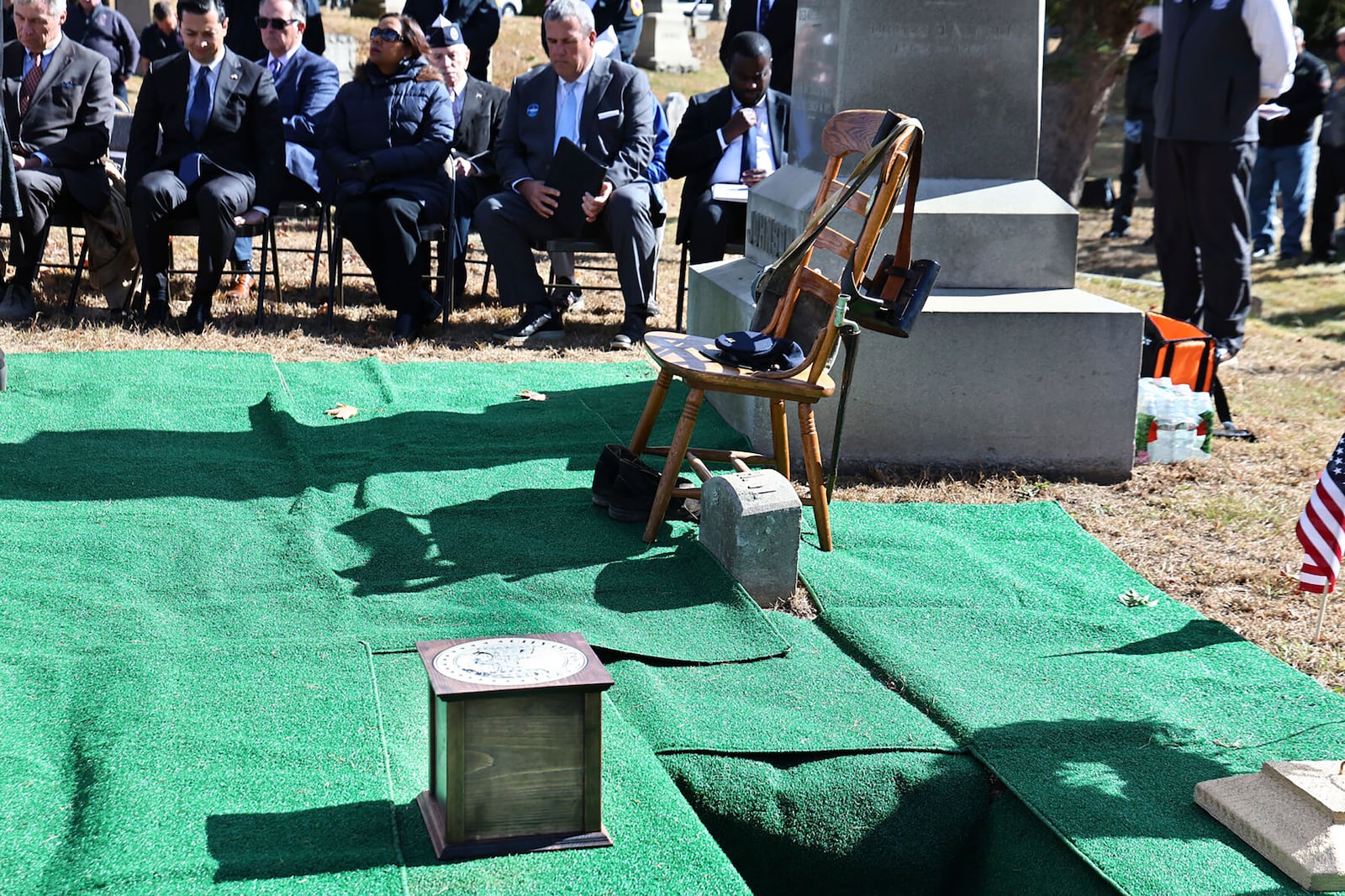 In this photo provided by The Valley Breeze, an urn, foreground, containing the cremated remains of Byron R. Johnson, a Union soldier who was born in Pawtucket, R.I., in 1844 and fought in the Civil War, rests at his burial site during funeral services, Wednesday, Oct. 16, 2024, at Oak Grove Cemetery, in Pawtucket, after his remains were transferred from storage at a cemetery in Seattle. (Charles Lawrence/The Valley Breeze via AP)