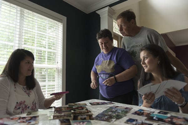 Jeannie Penland (center) and Jerry Penland, Amy Damera’s adoptive parents, look over childhood photographs with Katalina Jones (left) and Amy Damera (right) in Gainesville on May 5. Damera and Jones were each put up for adoption in Romania as children. When separate families took them in, the two didn’t know about each other — until recently. DAVID BARNES / DAVID.BARNES@AJC.COM