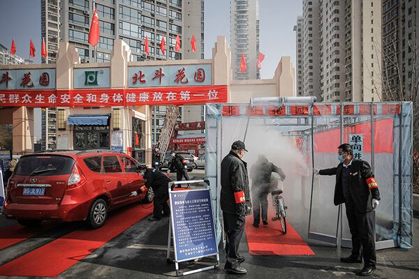 Security guards hold the curtain for a cyclist to past through a disinfectant spray Tuesday in order to return home at a residential complex in northern China's Tianjin Municipality.