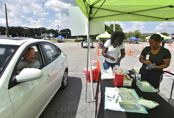 Ebonee Gresham (center) and Claudina Prince, both registered nurses with the DeKalb County Board of Health, prepare a flu shot for Tom Keating (left) of Decatur. HYOSUB SHIN / HSHIN@AJC.COM