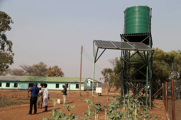 Villagers stand next to solar panels and water tanks that are part of a climate-smart agriculture program funded by the United States Agency for International Development in Chipinge, Zimbabwe on Thursday, Sept. 19, 2024. (AP Photo/Aaron Ufumeli)