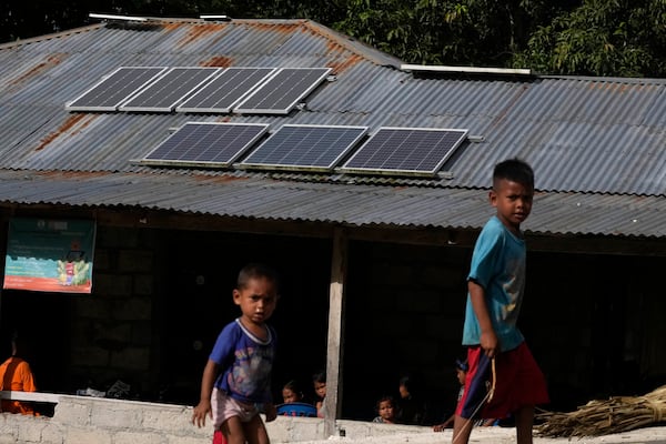 FILE - Children play near solar panels on the roof of house in Walatungga village on Sumba Island, Indonesia, March 21, 2023. (AP Photo/Dita Alangkara)