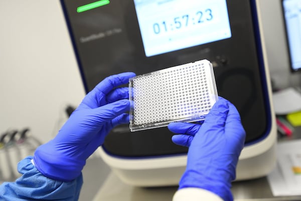 A lab worker holds a plate that will hold samples of possible COVID-19 and be put in the machine behind it to be analyzed at Ipsum Diagnostics labratory on Monday, March 23, 2020. JOHN AMIS /FOR THE AJC