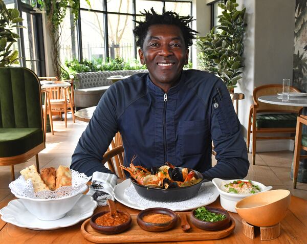 Executive chef Jean-Louis Sangare of Verdure Kitchen and Cocktails, shown with his recipe for Seafood Pepper Soup (in skillet), served with palm wine (in wooden bowl at right), focaccia bread (left), basmati rice with onions and chile pepper (right), and hot sauce, suya pepper and cilantro (in wooden tray, foreground, from left). (Styling by Jean-Louis Sangare / Chris Hunt for the AJC)