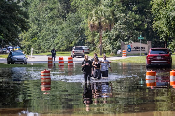 A group of people walk through a flooded road on Bradley Boulevard on Monday, August 12, 2024, in Savannah, Ga. (AJC Photo/Katelyn Myrick)