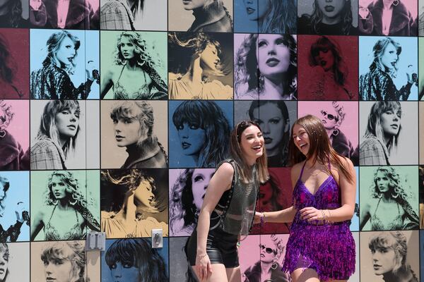 Wearing Taylor Swift attire, Megan Webb, left, of Smyrna, and Morgan Lewis, of Woodstock, react as they pose for a picture in front of the Taylor Swift merchandise bus at Mercedes-Benz Stadium, Friday, April 28, 2023, in Atlanta. Taylor Swift and Janet Jackson will perform next door to one another Friday night, Jackson at State Farm Arena and Swift at Mercedes-Benz Stadium. (Jason Getz / Jason.Getz@ajc.com)