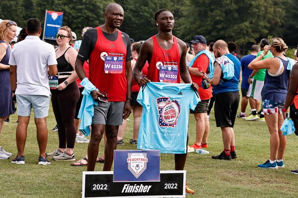 Dan Adhiambo (left) and his son James pose with  Peachtree Road Race t-shirts at Piedmont Park on Monday, July 4, 2022 (Natrice Miller/natrice.miller@ajc.com)