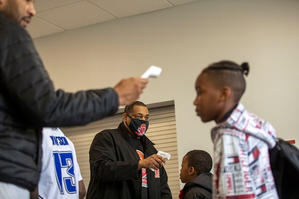 Kenneth Tarver, center, owner of KB Sports, takes a reading of a basketball player's temperature before allowing him to enter the Hebron Christian Academy gymnasium for a basketball game in Dacula last month. Tarver brought his own cleaning supplies, thermometers and bottles of hand sanitizer to the gym. (Alyssa Pointer / Alyssa.Pointer@ajc.com)