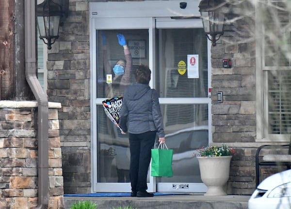 A worker unlocks the door at The Retreat at Canton as a visitor holds a birthday ballon at the front entrance. A family delivered the ballon and a gift bag to a relative at the assisted living community but could not go in after an outbreak of coronavirus there. Three residents and one employee have “tested presumptively positive” for COVID-19. (Hyosub Shin / Hyosub.Shin@ajc.com)