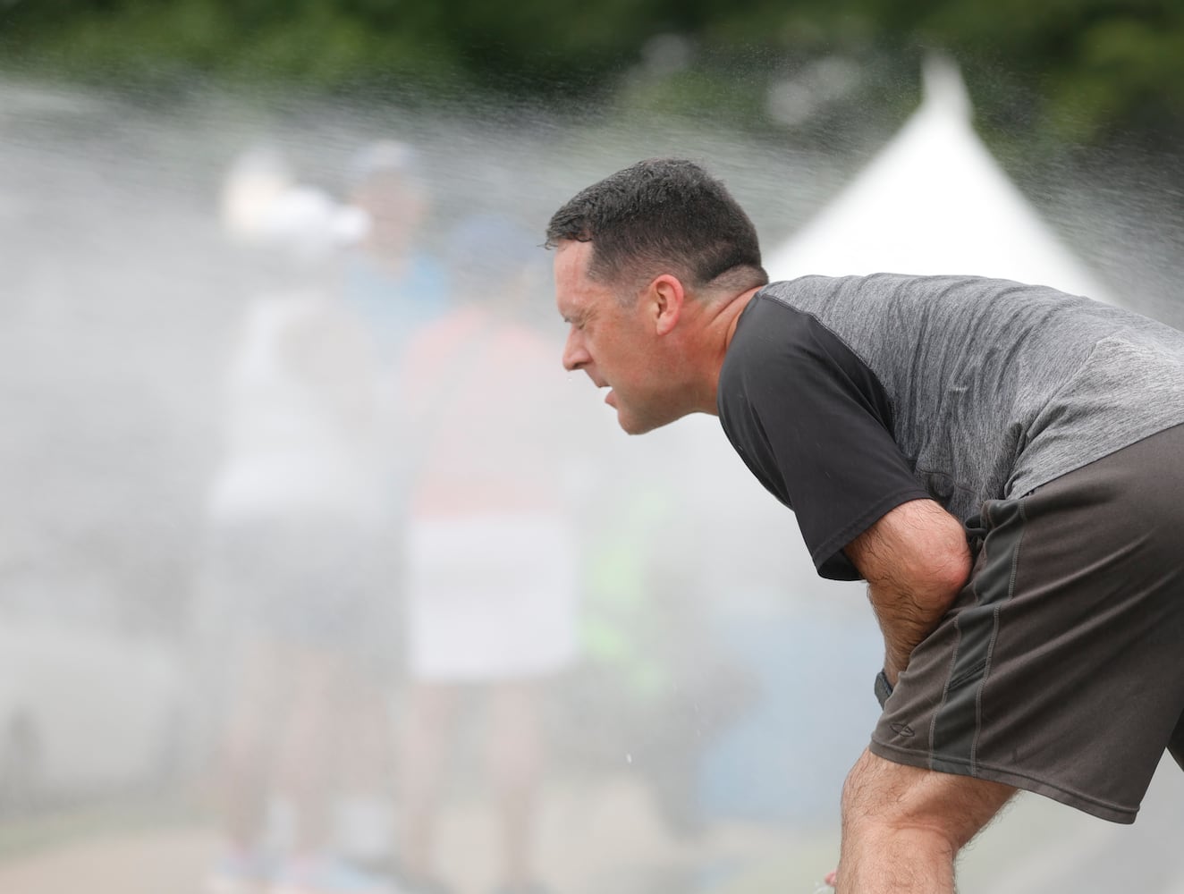 A runner cools off in the mist along Peachtree Street during the 54th running of the Atlanta Journal-Constitution Peachtree Road Race in Atlanta on Tuesday, July 4th, 2023.   (Natrice Miller / Natrice.Miller@ajc.com)