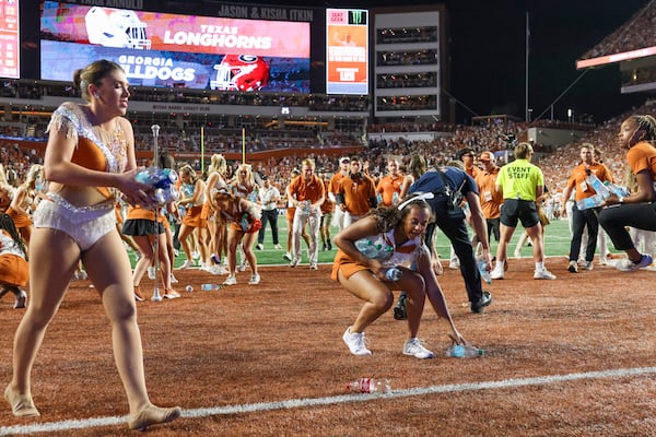 Texas students and cheerleaders pick up plastic bottles thrown by Texas fans as they reacted to a call by officials that negated a Texas interception during their game against Georgia at Darrel K Royal Texas Memorial Stadium, Saturday, October 19, 2024, in Austin, Tx. The call was reversed and the interception stood. (Jason Getz / AJC)

