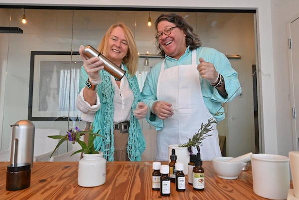 Jillian Cooke, founder of WWYW, shakes a spray bottle to mix natural sanitizer they just made as her husband John Cooke smiles at Wellness Within Your Walls (WWYW) in Buckhead on Friday, March 27, 2020. (Hyosub Shin/Hyosub.Shin@ajc.com)