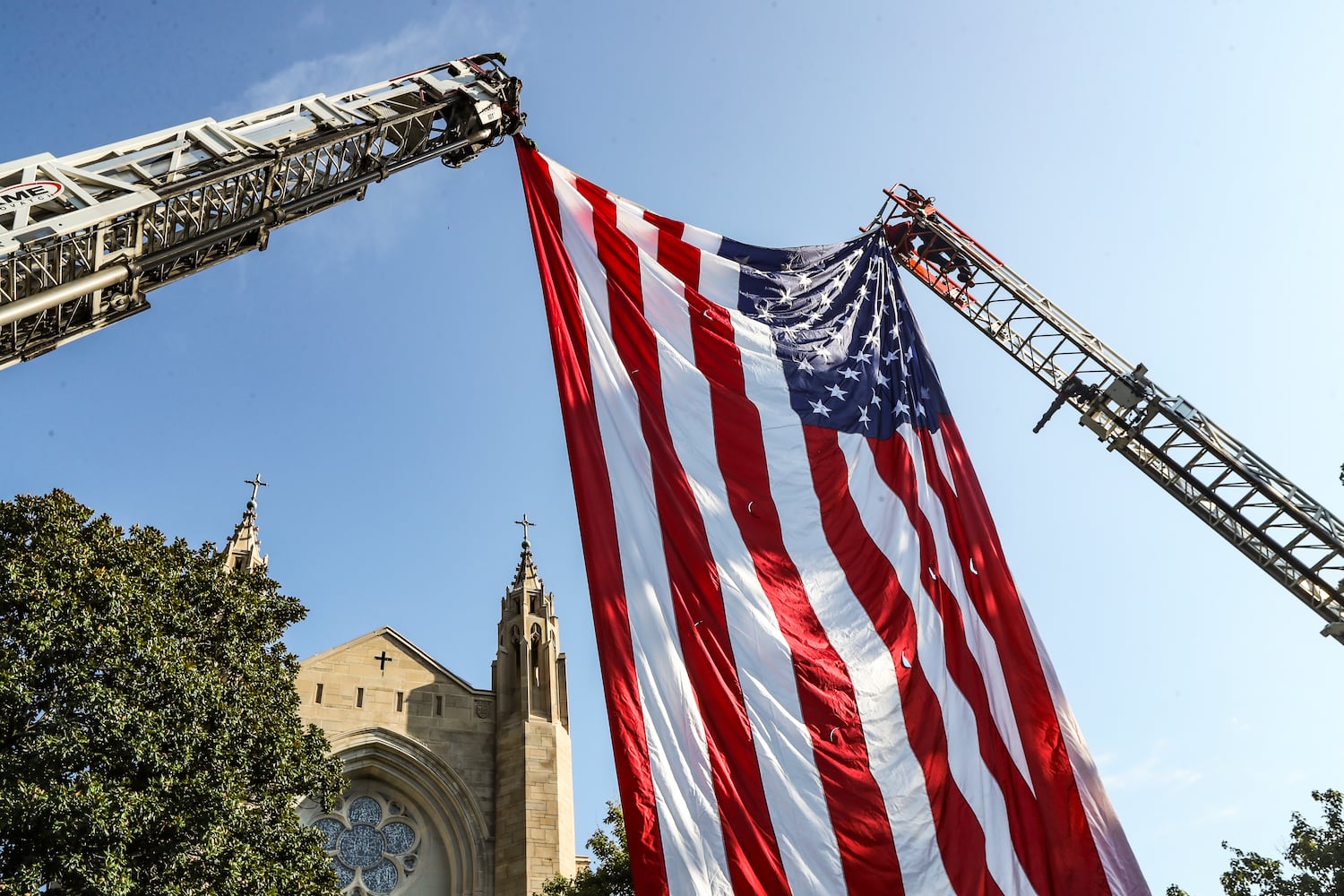 September 11, 2023 Atlanta: Atlanta firefighters post  a giant American flag between ladders at the Cathedral of Christ the King. Atlanta police and firefighters were in attendance on Monday, September 11, 2023 at the Cathedral of Christ the King, 2699 Peachtree Road, NE in Buckhead in observance of the Blue Mass. The annual Mass honors public safety officials and first responders. City of Atlanta Mayor, Andre Dickens, along with police, fire officials and honor guards participated in the solemn Mass led by Rector, Monsignor Francis G. McNamee. Wreaths were posted in front of the of the church, honoring those who lost their lives on Sept. 11, 2001. The Blue Mass tradition began in 1934, when a priest from the Archdiocese of Baltimore, Father Thomas Dade formed the Catholic Police and Firemen’s Society. (John Spink / John.Spink@ajc.com)

