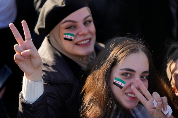 Syrian women flash victory signs with the colour of "revolutionary" Syrian flag on their faces, during a celebratory demonstration following the first Friday prayers since Bashar Assad's ouster, in Damascus' central square, Syria, Friday, Dec. 13, 2024. (AP Photo/Hussein Malla)