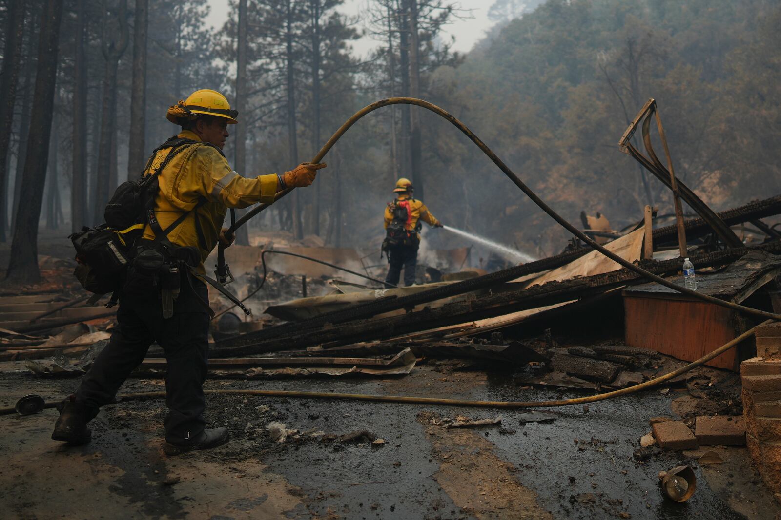 Firefighters hose down hot spots on a fire-ravaged property while battling the Bridge Fire Wednesday, Sept. 11, 2024, in Wrightwood, Calif. (AP Photo/Eric Thayer)