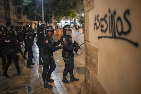 Riot police walks by a graffiti reading in spanish "murderers" during minor clashes after a peaceful protest organized by social and civic groups, denouncing the handling of recent flooding under the slogan "Mazon, Resign," aimed at the president of the regional government Carlos Mazon, in Valencia, Spain, Saturday, Nov. 9, 2024. (AP Photo/Emilio Morenatti)