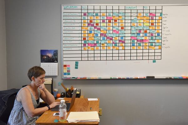 Julie Wilson, executive director of the AJC Decatur Book Festival, works on her computer as an appearance schedule of authors is displayed on a board at the festival’s new office in Decatur. HYOSUB SHIN / HSHIN@AJC.COM