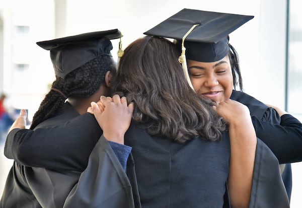 Carrie Crayton, left, and Natalie Jackson (right), both from the first graduating class of Georgia Tech’s EXCEL program for students with intellectual disabilities, get a hug from Rene Reese, right, career development coordinator, after they try on their caps and gowns. 