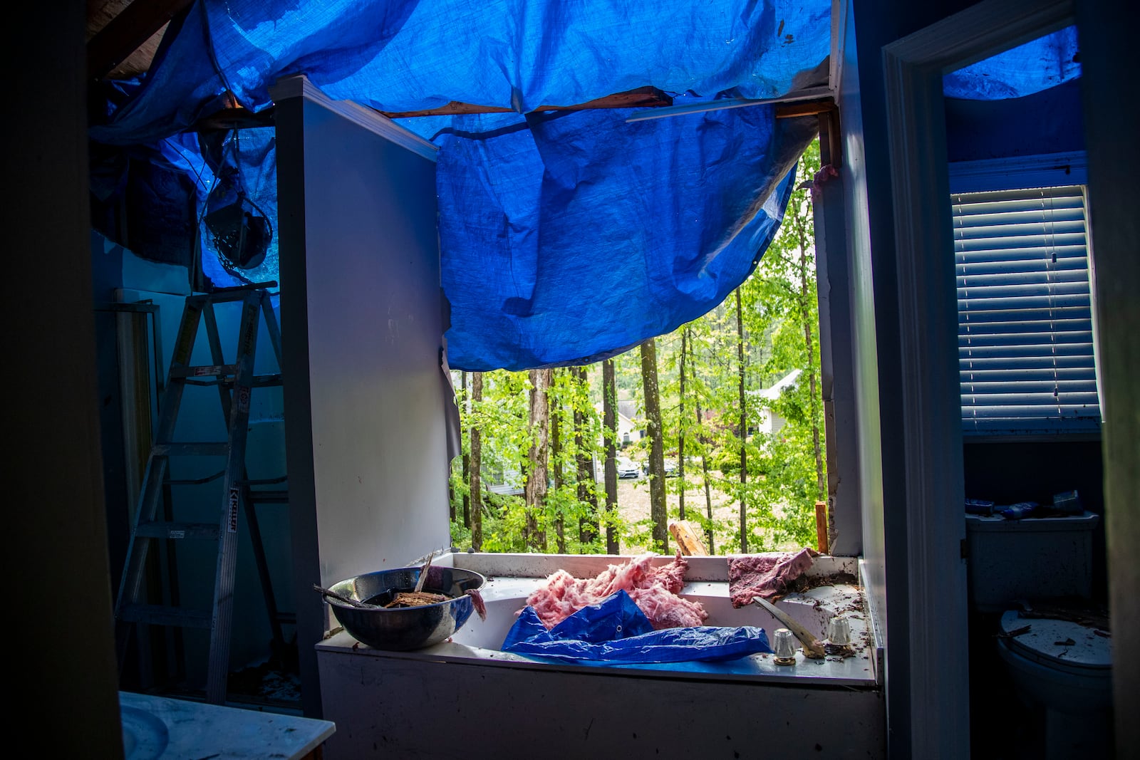 Sherell Lewis used a blue tarp to stop water from entering his house after a tree caused damage to the master bathroom in his southwest Atlanta neighborhood Monday.