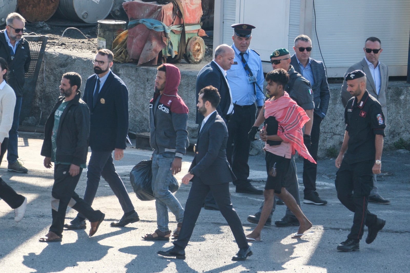 Migrant and security officials walk at the port of Shengjin, northwestern Albania. Wednesday, Oct. 16, 2024 after disembarking from the Italian navy ship Libra, carrying the first group of 16 migrants intercepted in international waters. (AP Photo/Vlasov Sulaj)