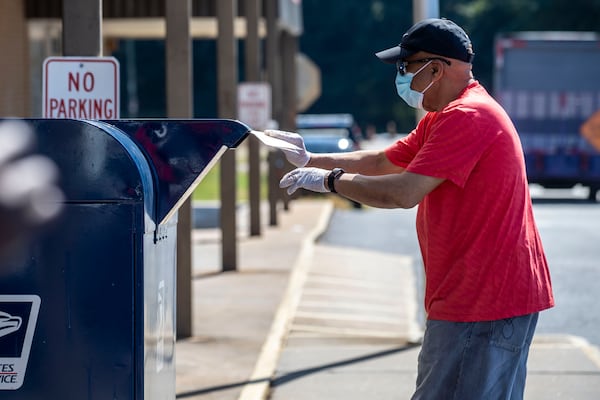 An individual deposits letters into a mailbox outside a post office in Decatur on Tuesday. The U.S. Postal Service, in a July 29 letter to Georgia Secretary of State Brad Raffensperger, recommended that voters request an absentee ballot at least 15 days before Election Day, and that they mail completed ballots at least one week in advance, by Oct. 27. (ALYSSA POINTER / ALYSSA.POINTER@AJC.COM)