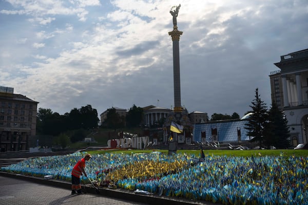 A cleaner sweeps a sidewalk in front of a memorial site honoring people killed in the war in Independence Square in Kyiv, Ukraine, Monday, July 3, 2023. (AP Photo/Jae C. Hong)