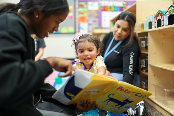 Eighth grade student Mia Avouwadan reads the book "Pete the Cat" to 20-month-old Daniela Trevino at the Play 2 Learn program at Duluth Middle School, Wednesday, Nov. 8, 2023. Daniela’s mother Ilse Trevino is shown at right. These students are part of the teaching profession program and have an interest in a career in education. (Jason Getz / Jason.Getz@ajc.com)