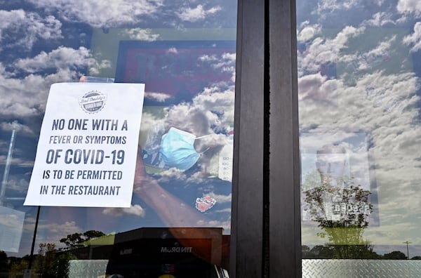 April 25, 2020 Decatur - Julian Douglas, employee, posts a warning sign at the main door as restaurant staff prepare to reopen the restaurant at Bad Daddy's Burger Bar in Decatur on Saturday, April 25, 2020. On Monday, Kemp announced shuttered businesses including barbershops, beauty and nail salons, spas, gyms and bowling alleys could reopen Friday. Movie theaters and restaurant dining rooms can reopen Monday. (Hyosub Shin / Hyosub.Shin@ajc.com)