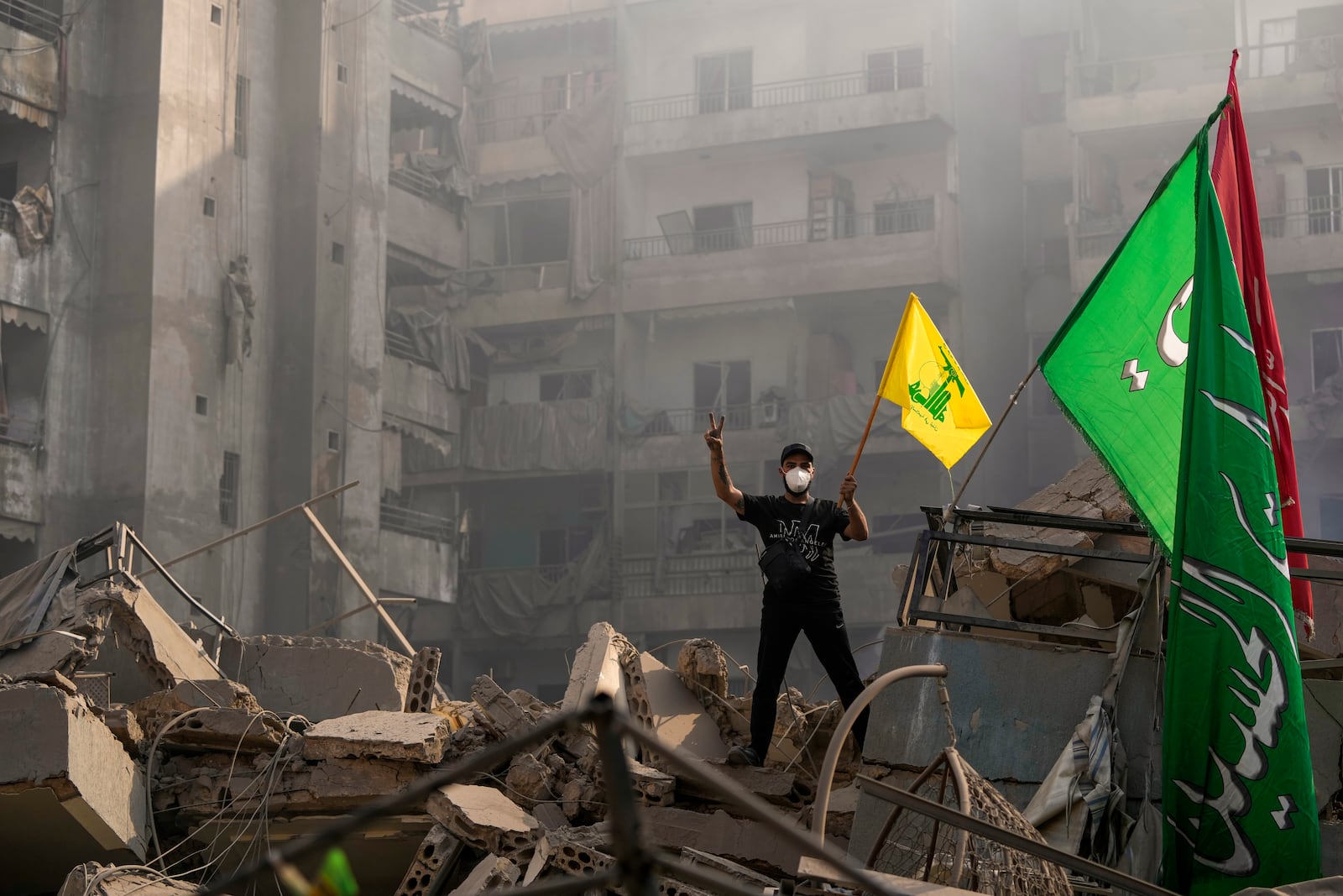 A man flashes the victory sign as holds up a Hezbollah flag while stands on the ruins of his destroyed apartment at the site of an Israeli airstrike in Dahiyeh, Beirut, Lebanon, Friday, Nov. 1, 2024. (AP Photo/Hassan Ammar)