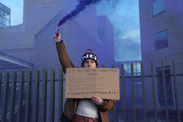 A woman fires a flare outside the Palace of Justice during a women's rights demonstration, Saturday, Dec. 14, 2024 in Avignon, southern France, where the trial of dozens of men accused of raping Gisèle Pelicot while she was drugged and rendered unconscious by her husband is taking place. (AP Photo/Aurelien Morissard)