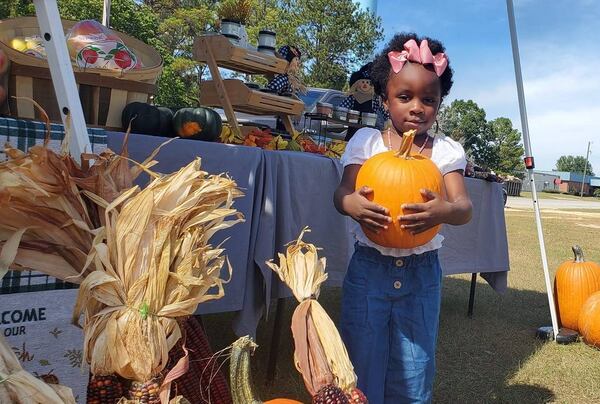 A young girl carries a pumpkin at the International City Farmers Market in Warner Robins. The market helps feed the homeless thanks to owner Joshua Hess. (Photo Courtesy of Joshua Hess)