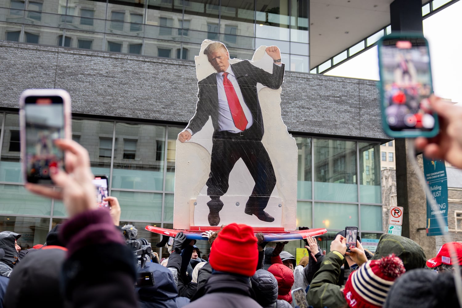 People waiting to enter a Trump rally at Capital One Arena in Washington, D.C. pass around a Trump cutout on a surfboard on Sunday, January 19, 2025, one day before Donald Trump’s inauguration. Attendees said the cutout was surfing the red wave to drain the swamp. (Arvin Temkar / AJC)