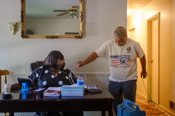 Milledge Perrymond, right, makes adjustments to Latoshia Allen Perrymond’s oxygen machine at their Stone Mountain home. Latoshia Perrymond is participating in a long COVID study with the National Institutes of Health. (Arvin Temkar / arvin.temkar@ajc.com)