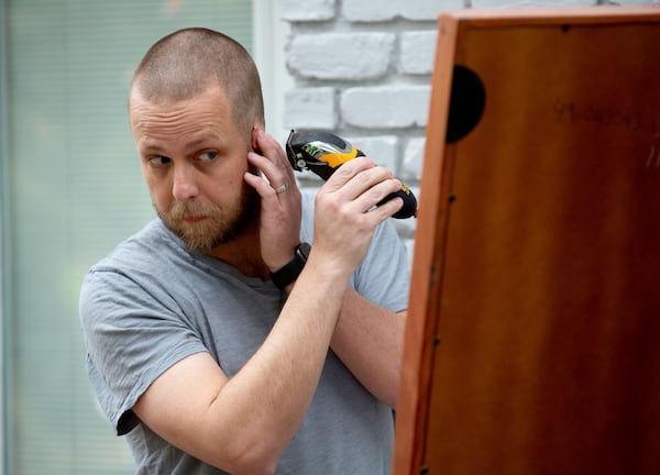 Dan Parker cuts his own hair on the porch of his Atlanta home last week. He says he resorted to his “summer dad” vibe  to remind him of summers as a boy when his parents would shave his head for camp. (STEVE SCHAEFER FOR THE ATLANTA JOURNAL-CONSTITUTION)